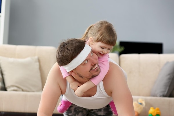 daughter riding horsey on the back of her dad as he is exercising