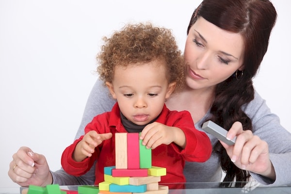 Babysitter guiding a child with block building spacial play