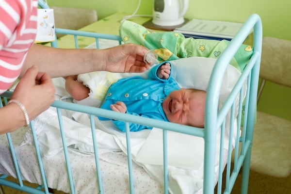Crying baby in a bassinet with parent unsuccessfully trying to sooth him with a pacifier 
