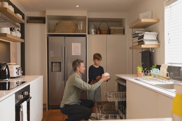 Father teaching his young son how to correctly load a dishwasher.