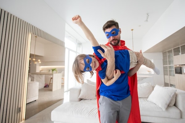 Father and young son dressed as super heroes with dad holding the flying boy