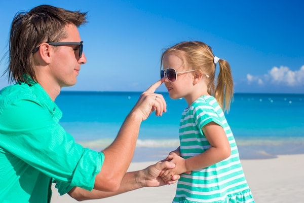 Father putting sunscreen on daughter's nose during a beach vacation