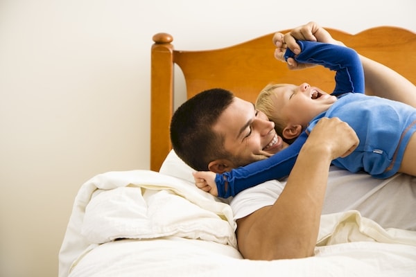 Father rough-housing with son on bed during a tickle session