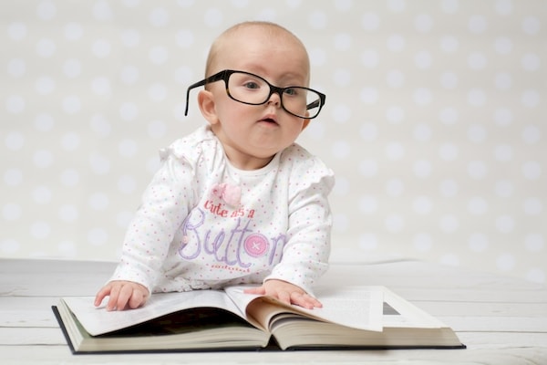 Young infant looking studious wearing eye glasses and pretending to read a book