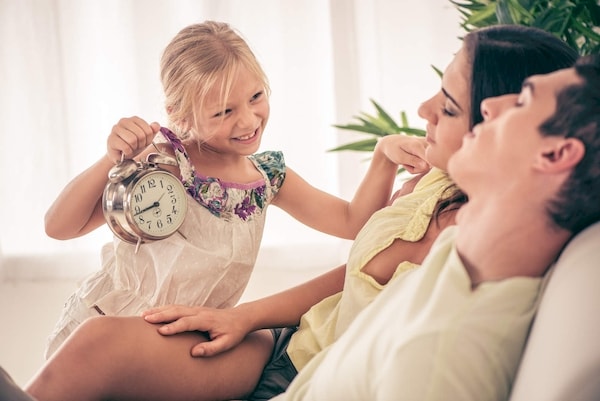 Smiling youngster waking her parents up in the very early morning holding an alarm clock