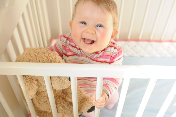 Smiling toddler standing in his crib looking like he wants out 